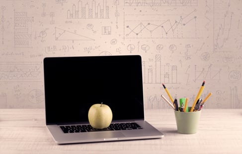 Close up of white business office desk with laptop tablet in front of brown wall background full of pie charts and numbers